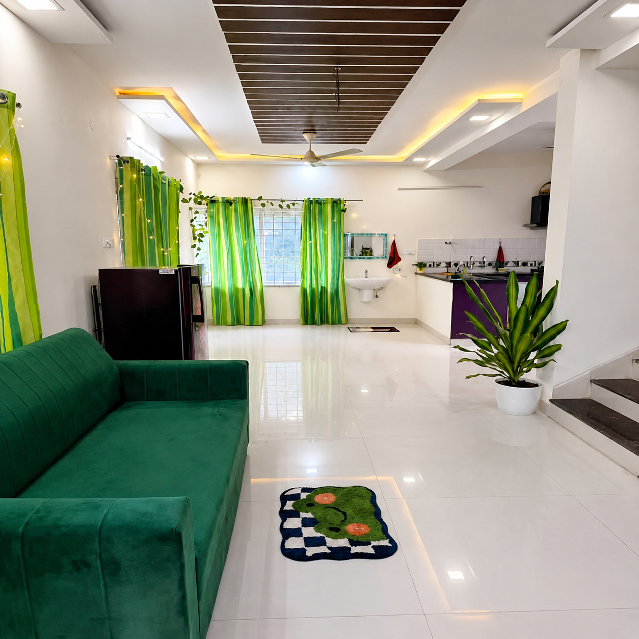 Modern living room, spacious living room, contemporary home interior, stylish living space, bright living room, open plan interior, green sofa, velvet sofa, comfortable sofa, elegant sofa design, glossy white flooring, tiled floor, modern ceiling design, false ceiling, wooden ceiling panels, LED ceiling lights, warm ambient lighting, ceiling fan, large windows, natural light, green curtains, striped curtains, indoor plants, potted plants, decorative greenery, compact kitchen, open kitchen, modular kitchen, purple kitchen cabinets, black countertop, modern sink, dining and cooking area, staircase, modern staircase, stainless steel railing, glass railing, clean home interior, organized living space, apartment interior, residential property, urban home, student-friendly accommodation, student living space, student rental home, business professional accommodation, working professional home, professional living space, comfortable rental home, practical home design, modern real estate interior.